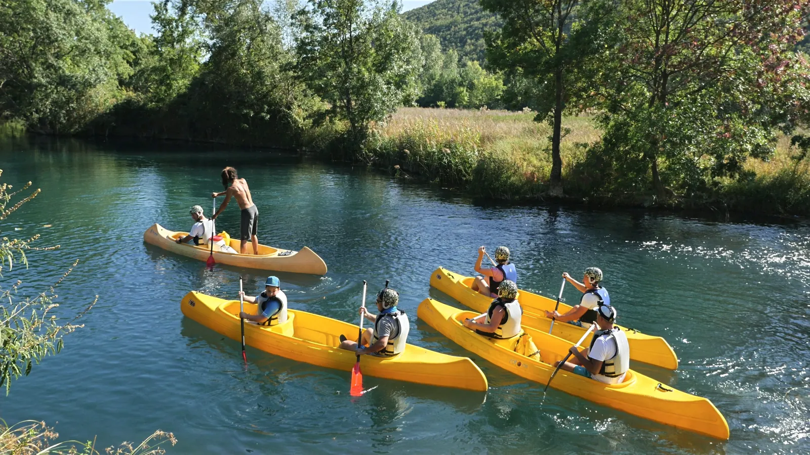 Five yellow canoes with paddlers on a turquoise river