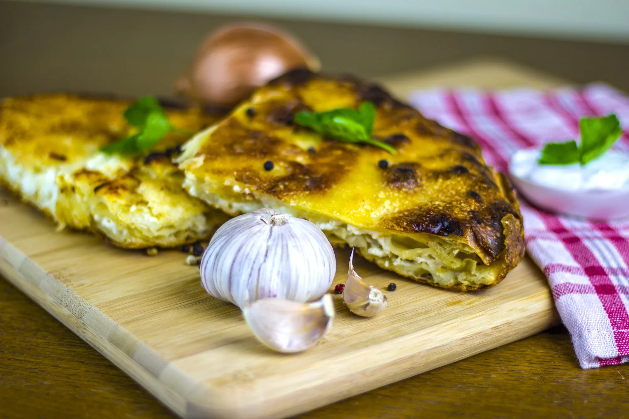 Freshly baked Albanian bërek on a board with garlic and yoghurt